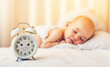 © Віталій Рудь - A baby is sleeping on a bed with a white clock on the bedside table