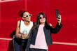 © VISTA by Westend61 - Young friends taking selfie through smart phone near red background