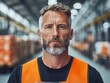 © Sergey - A man in an orange safety vest stands confidently in a modern factory setting, holding a tablet. The industrial background reflects a focus on technology and efficiency.
