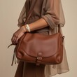 © Tatyana - Woman with brown leather crossbody bag against neutral background.
