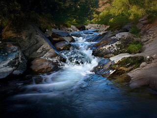 Poster - Serene mountain stream flows over smooth rocks, creating a tranquil scene with lush greenery.  The water is clear and blue, reflecting the sunlight.