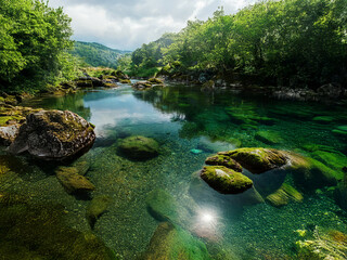 Poster - Serene river scene: crystal-clear water reveals the riverbed, moss-covered rocks, and lush green banks under a partly cloudy sky.  Sunlight glints on the surface.