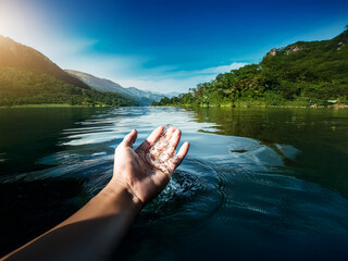 Poster - A hand reaches out from the water, touching the surface of a calm river surrounded by lush green mountains under a vibrant sky.  The scene evokes peace and serenity.