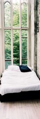 Canvas Print - White bed near large window overlooking green trees.