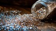 © bulegendut - Glittering gold and silver sprinkles spilling from a glass jar onto a wooden surface.
