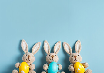 Wall Mural - three plush bunnies holding colorful easter eggs on a light blue background create a festive spring 