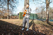 © Fauren - Young man leaning against a tree, playing an acoustic guitar in a sunlit autumn park, surrounded by fallen leaves and nature’s vibrant colors, creating a serene atmosphere