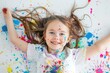 © Alexandr Efimov - The image shows a joyful child with long hair, covered in vibrant paint splatters from creative play outdoors. The scene is full of life and color.