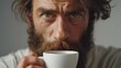 © Oleg - A bearded man pausing to enjoy a cup of coffee, contemplative gaze. Photograph capturing an intimate, candid moment.