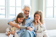 © Юлия Завалишина - Happy family at home. Two little girls sisters twins grandmother enjoying time together watching video on phone. Good time at home. Grandma granddaughters child kids together. Family generations