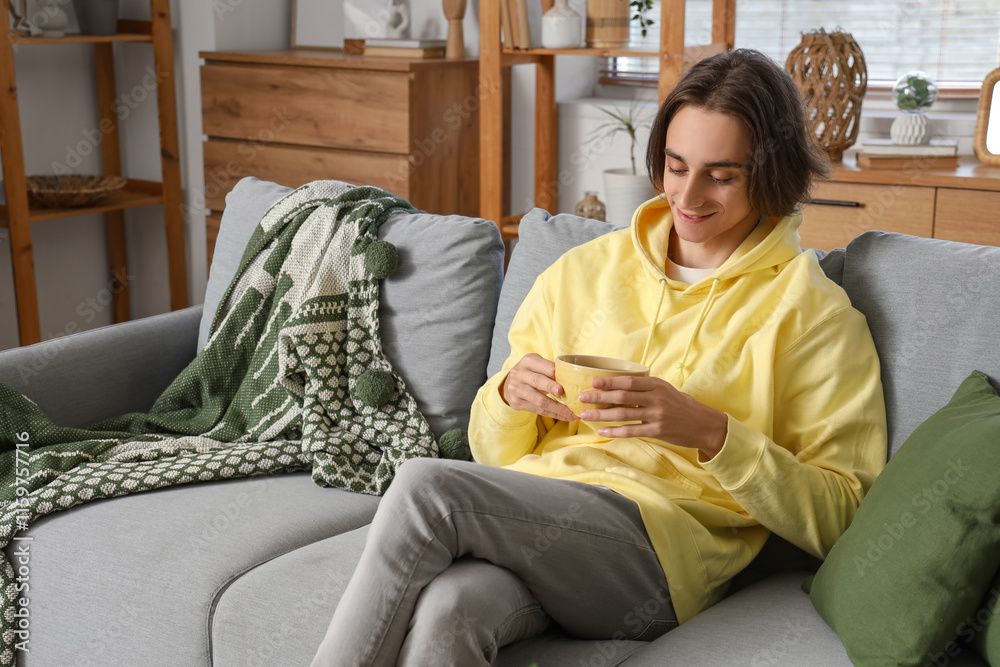 Young man with cup of tea sitting on sofa at home