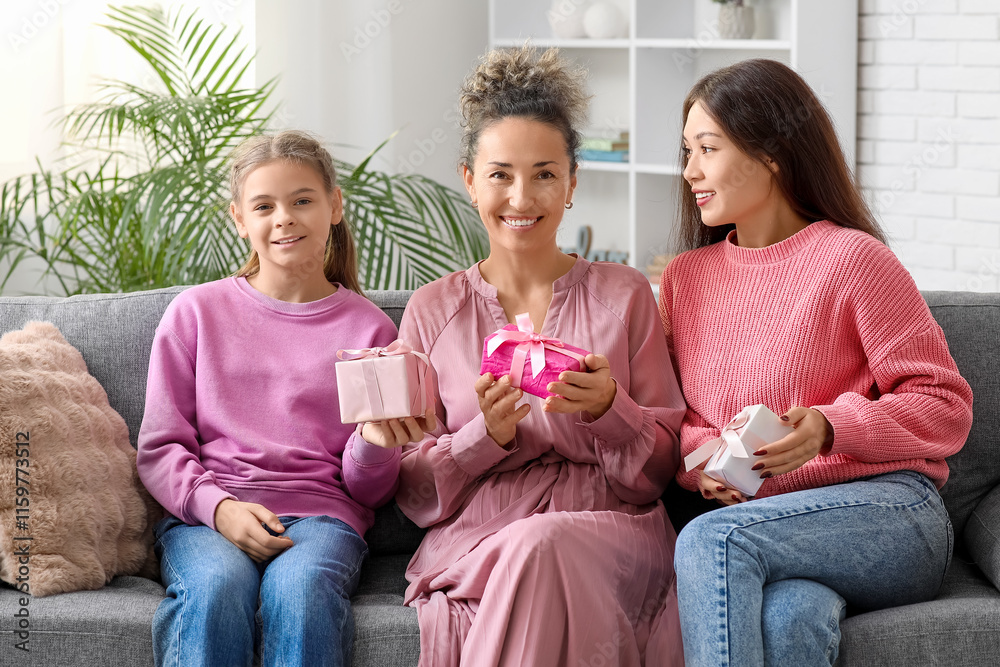 Mature woman and her daughters with gift boxes sitting on sofa at home