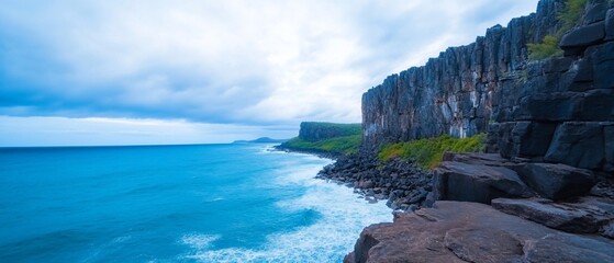 Wall Mural - Cliffside view of ocean with blue water and cloudy sky.