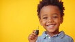 © EFA - A smiling child holding a small object against a bright yellow background.
