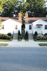 Charming Duplex: A charming white duplex home with a lush green lawn and blooming flowers, bathed in the warm glow of a summer afternoon.  This quaint property exudes a sense of peace and tranquility.