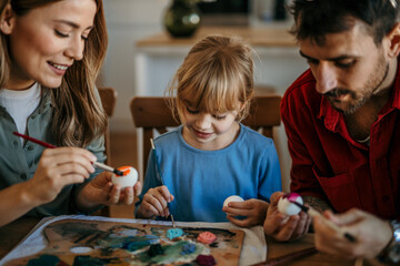 Wall Mural - Family laughter as they enjoy decorating eggs with brushes and stickers for Easter celebration