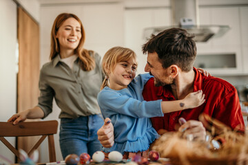 Wall Mural - Happy family gathered around the table painting colorful Easter eggs in their cozy dining room