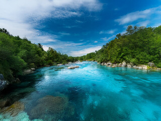 Poster - A vibrant river flows through a lush green valley under a bright blue sky.  The water is incredibly clear, revealing the rocks below.
