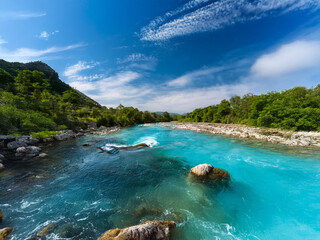 Poster - A vivid turquoise river flows through a lush green valley under a bright blue sky.  The water is crystal clear, revealing rocks below.  A peaceful and scenic landscape.