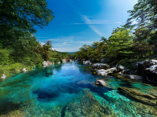 Poster - A serene, crystal-clear river flows through a lush green landscape under a vibrant blue sky.  The water's clarity reveals the riverbed below.  The scene is peaceful and idyllic.
