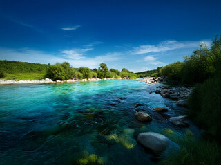 Poster - Serene river scene under a vibrant blue sky.  Crystal-clear water flows over smooth river rocks, lush greenery lines the banks.  Peaceful, idyllic landscape.