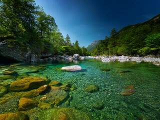 Poster - Serene mountain river scene. Crystal-clear turquoise water flows over smooth rocks, lush green vegetation lines the banks under a vibrant blue sky.  A tranquil, idyllic landscape.