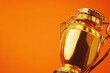 © Alla - A golden trophy sitting on an orange background, perfect for awards or recognition scenes