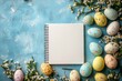 © c80 - Colorful Easter eggs arranged around a blank notebook on a light blue surface with floral accents