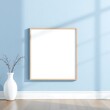 © Michel - Modern Minimalist Interior Mockup: A clean and stylish photo mockup featuring a blank canvas in a wooden frame, set against a light blue wall with natural light streaming through a window.
