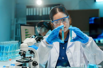 Wall Mural - scientist wearing lab coat and gloves comparing two test tubes with blue liquid during medical resea