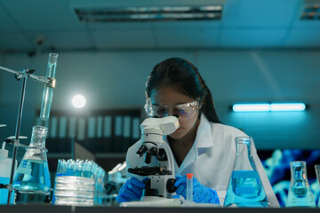 Wall Mural - female scientist using a microscope analyzing sample in laboratory glassware with blue liquid for me
