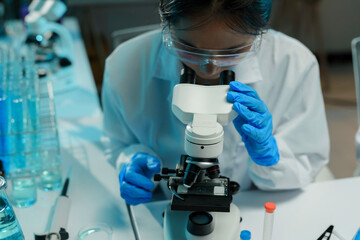 Wall Mural - female scientist wearing protective glasses and gloves using microscope, analyzing sample in laborat
