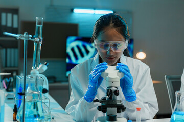 Wall Mural - asian female scientist using a microscope in a laboratory at night, developing innovative medicine f