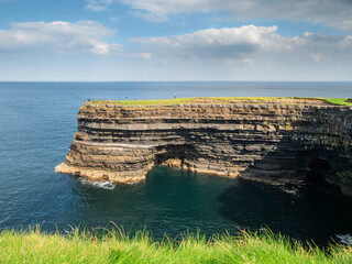 Rough stone coast line with cliff and blue ocean and blue sky. Downpatrick head, Ireland. Warm sunny day. Travel and tourism. Stunning Irish nature landscape scenery.