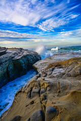 Wall Mural - 2023-12-31 A ROCKY OUTCROPPING IN LA JOLLA CALIFORNIA WITH WAVES CRASHING FROM THE PACIFIC OCEAN WITH A BEAUTIFUL CLOUDY BLUE SKY NEAR SAN DIEGO