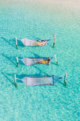 Wall Mural - hammocks sway gently over the turquoise waters of Koh Kood, inviting relaxation in a ropical paradise. Sunlight glistens on the waves, a couple of men and a woman relaxing in hammock in the ocean