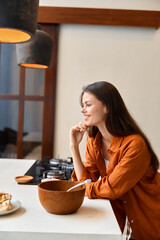 Canvas Print - Young woman in a cozy kitchen during fall, smiling as she prepares a healthy meal with a wooden bowl, showcasing vibrant autumn colors and a warm atmosphere