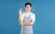 © STOCK88PHOTOGRAPHER - Portrait of young Asian man wearing apron and posing on blue background