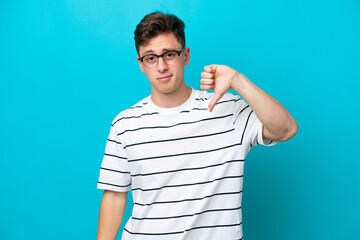 Wall Mural - Young handsome Brazilian man isolated on blue background showing thumb down with negative expression