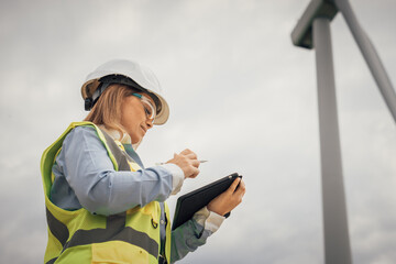 Poster - A female engineer is currently inspecting a renewable energy site, using her tablet to monitor various aspects of the project, demonstrating her skills and expertise in technology and sustainability