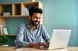 © miss irine - Smiling Indian man works on laptop in home office. Happy adult focused on work online learning session. Man uses computer at home office. Seems involved in online class virtual training session.