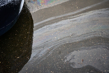 Wall Mural - Gasoline or oil spill creating rainbow sheen on asphalt parking lot near car