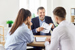 © Studio Romantic - Realtor or real estate agent discusses a new home plan with a family couple during a meeting in an office. Conversation focuses on the property purchase, planning and decision-making in real estate.
