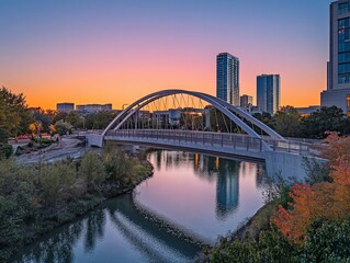 Wall Mural - Sunset view of modern arched bridge over calm river with cityscape background.