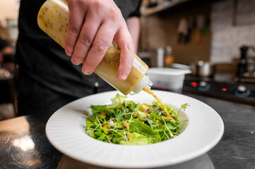 Wall Mural - A chef drizzles a flavorful dressing over a fresh green salad in a stylish kitchen. The dish showcases vibrant greens, emphasizing freshness and culinary expertise. Perfect for food-related content.