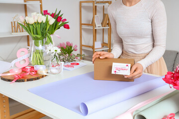 Poster - Woman with gift box, packing materials and beautiful tulip flowers at light table. International Women's Day