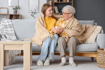 Wall Mural - Happy senior woman and her granddaughter with plaid drinking tea on sofa at home