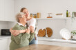 © Pixel-Shot - Happy senior woman and her granddaughter hugging in kitchen at home