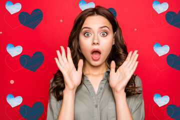 Wall Mural - Close up portrait brunette lady with cool hairstyle, big eyes and palms near face look at camera isolated on vivid red background