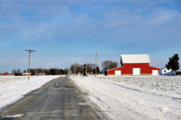 a red barn sits next to a field dusted with snow along a lonely contry road on the first day of wint